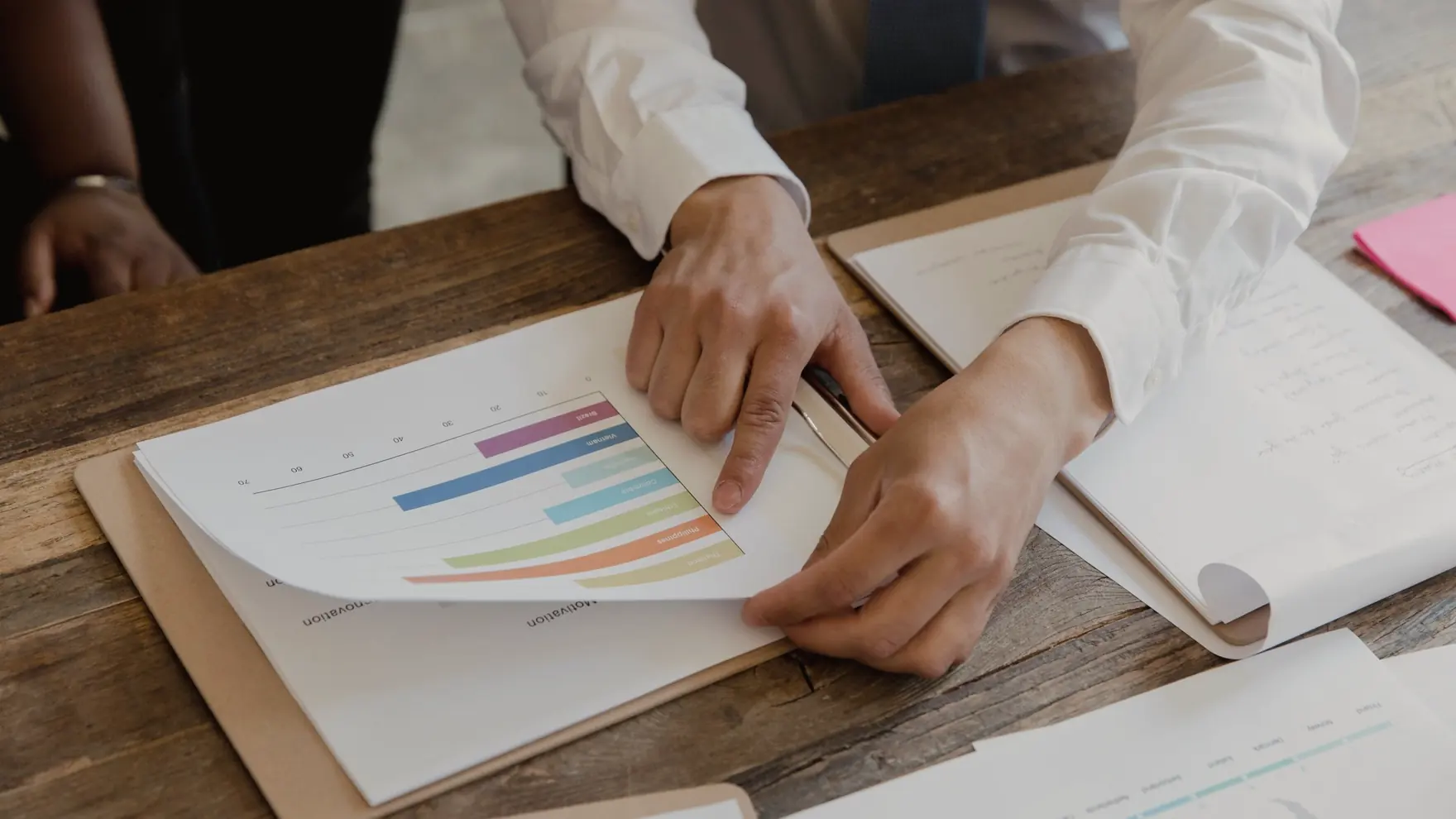 Hands holding a printed report with a bar chart on a wooden meeting table
