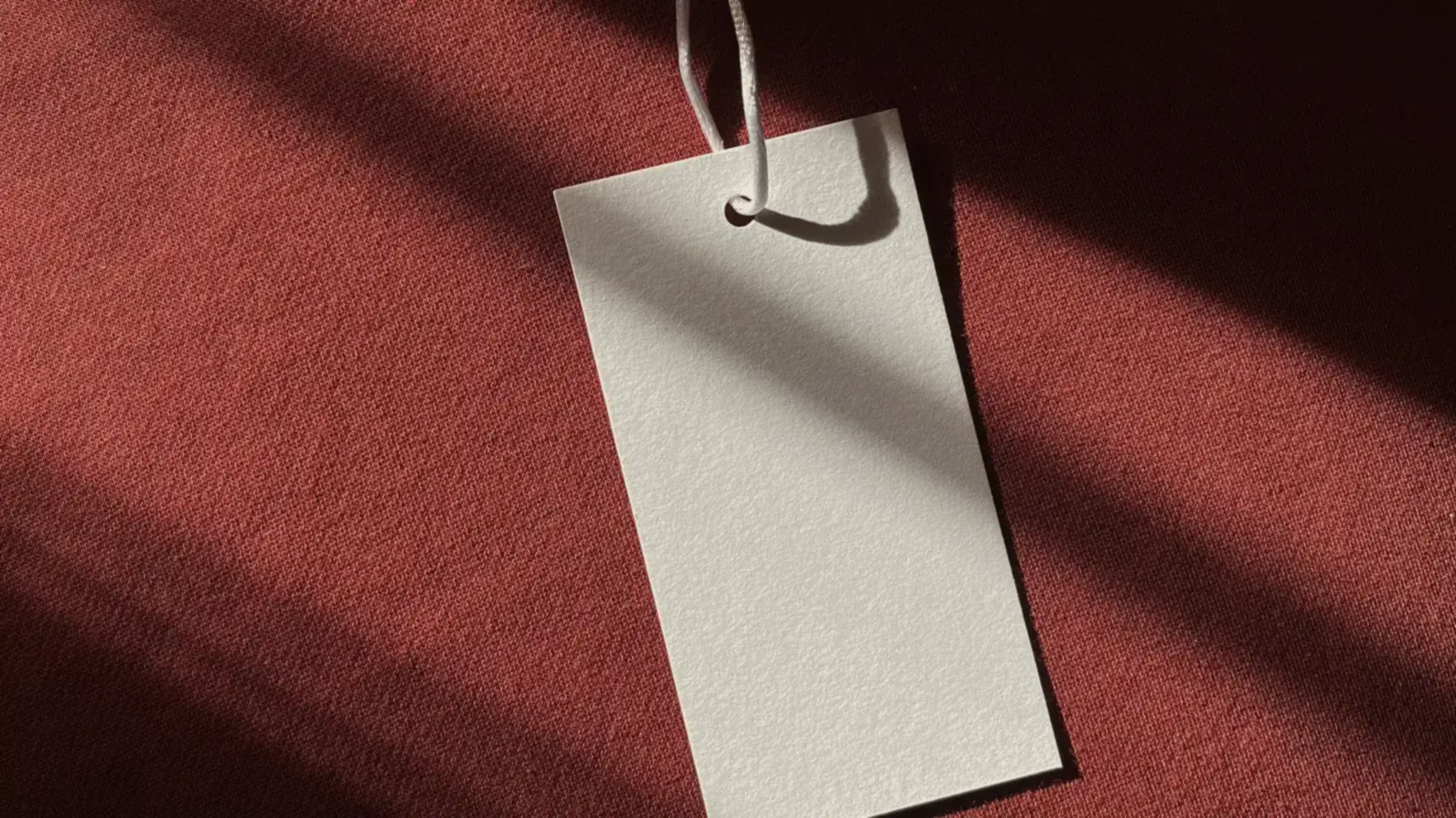 A blank price tag hanging on a red garment in low sunlight